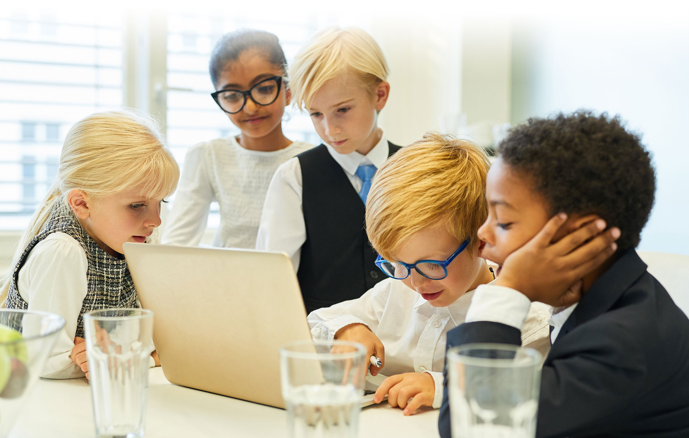 Children in business attire in meeting around laptop