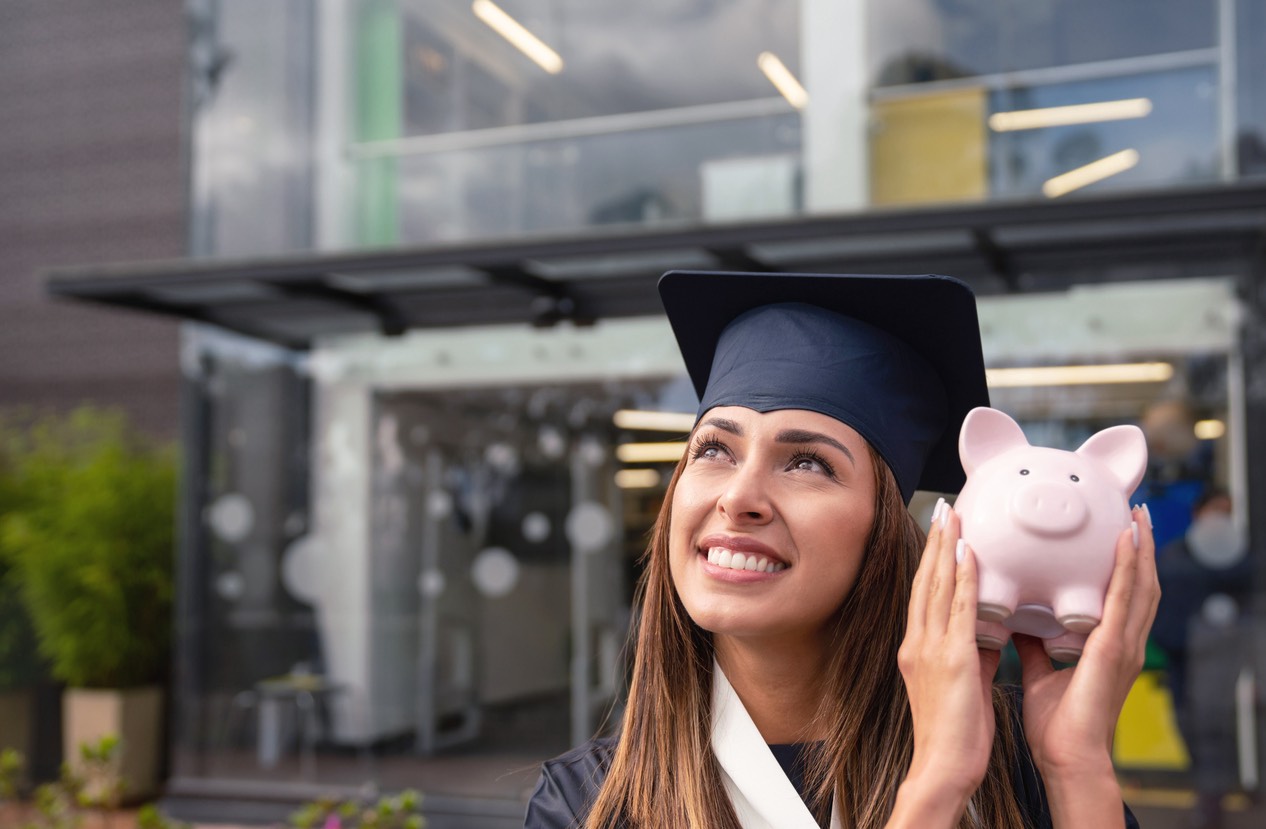 female college graduate holding up piggy bank