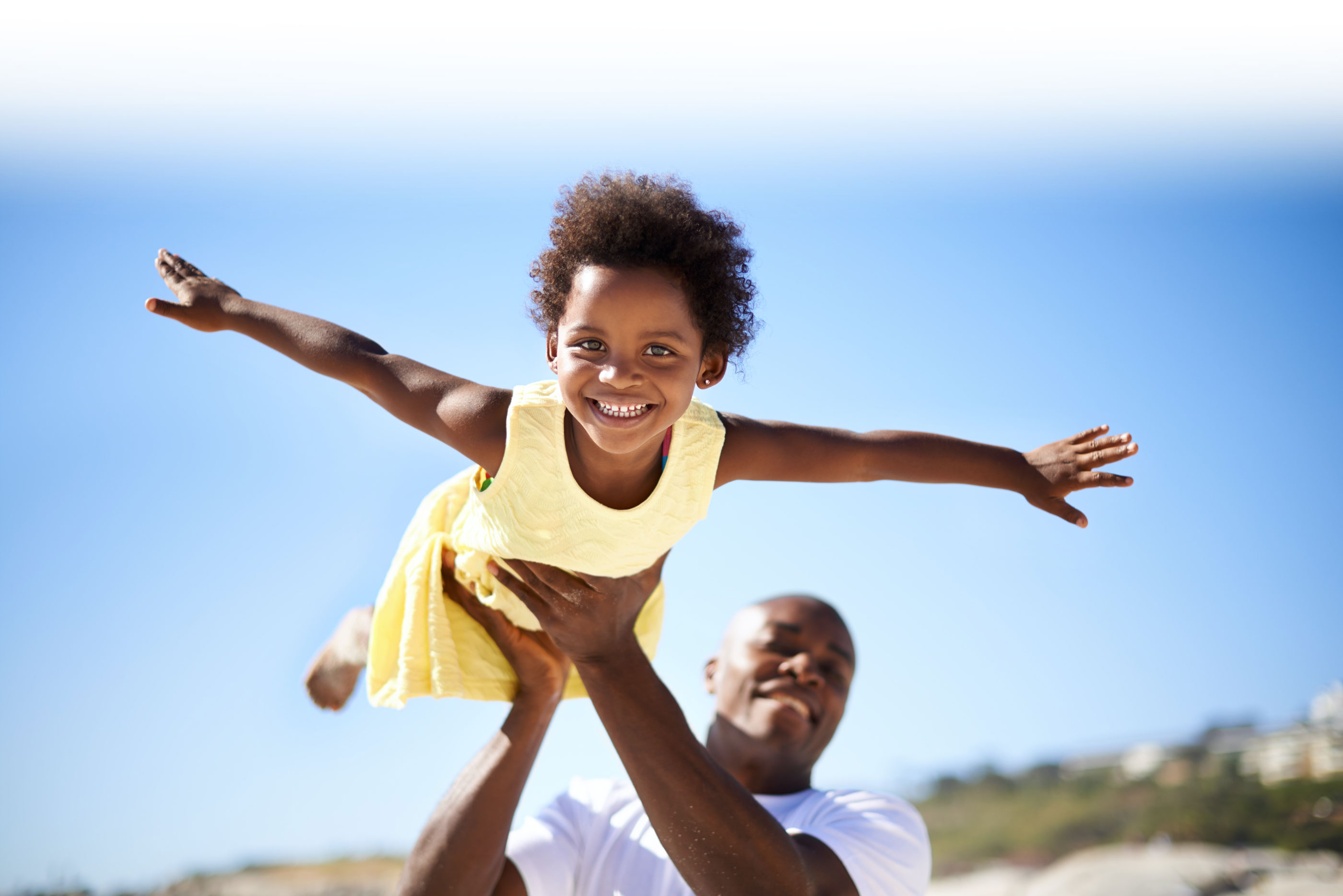 Dad holding up daughter in flying pose with clear sky background